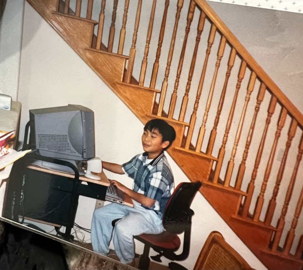 A childhood photograph of Tan sitting at a desktop computer under a staircase.